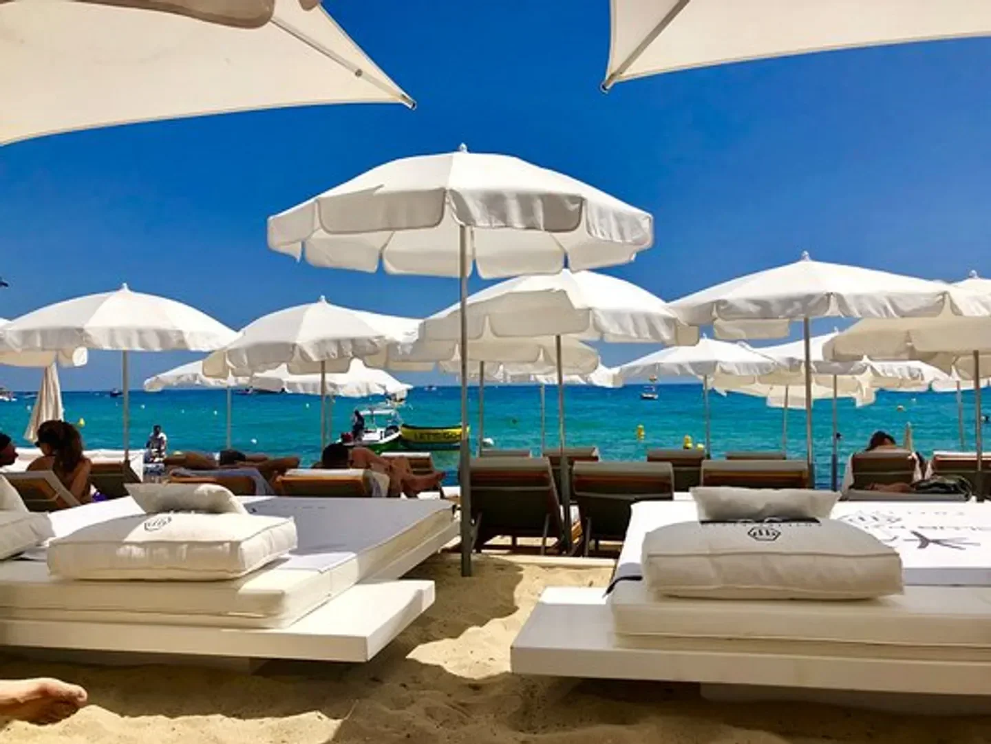 Beach scene at Clubs Les Palmiers in Saint-Tropez with white umbrellas and sunbeds.