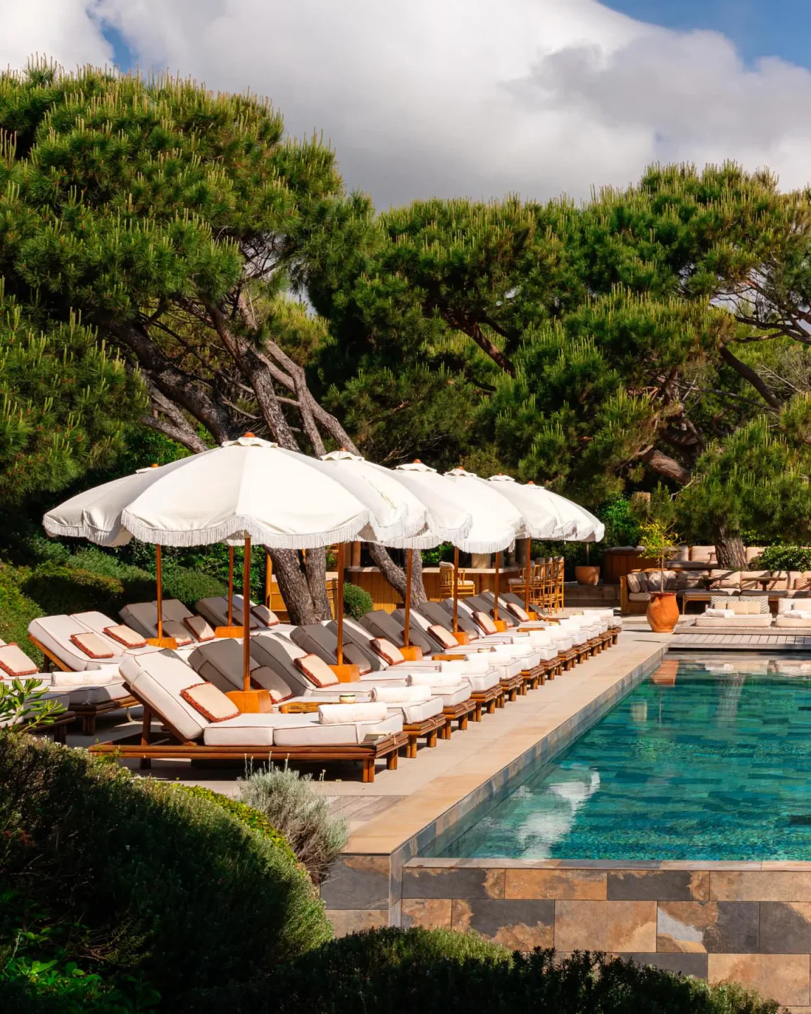 Gigi Ramatuelle Saint-Tropez poolside loungers and umbrellas with lush green trees overhead.
