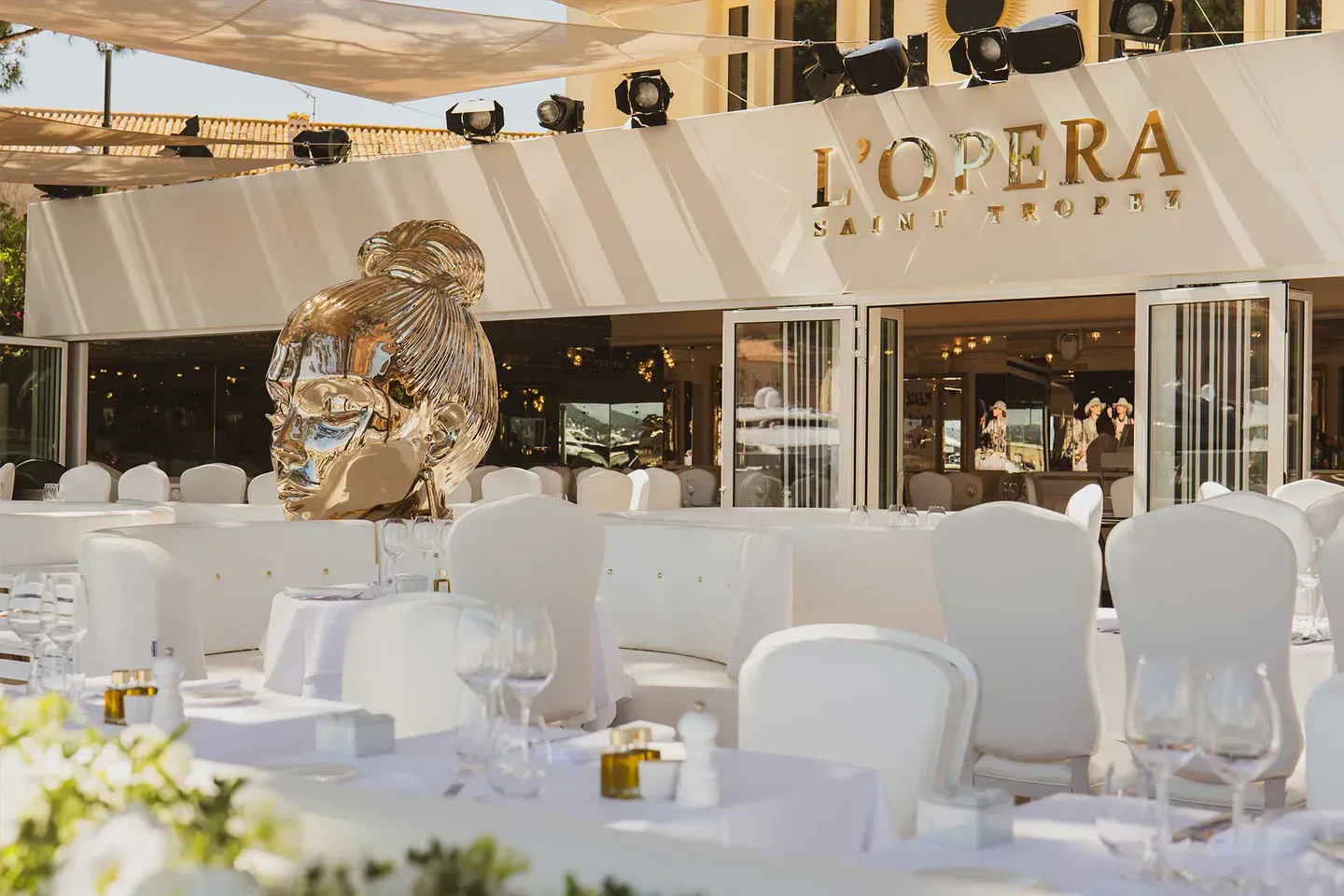 Outdoor dining at L'Opera Saint-Tropez restaurant with art sculpture and white decor